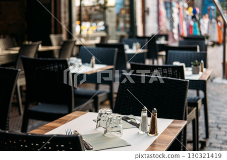 Modern cafe terrace with neatly arranged tables and chairs on a cobblestone street. Urban calm, quiet luxury, soft minimalism, refined casual dining 130321419