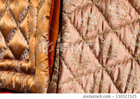 Close-up of ornate quilted fabrics in rich tones and baroque floral patterns hanging in sunlight. Maximalist decor, secondhand textiles, brocade revival, retro fabric trends 130321525