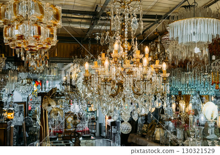 Ornate antique chandeliers and glass lighting fixtures densely displayed in a flea market interior. Vintage lighting, decorative reuse, secondhand interiors, opulent sustainability 130321529