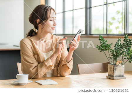 Young Asian woman looking at her smartphone while drinking coffee in a cafe (meeting) 130321661