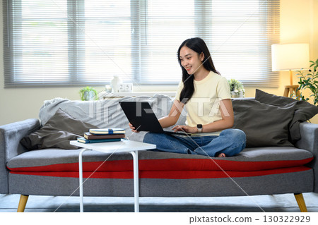 Relaxed Asian woman using a laptop in a cozy living room with natural light Relaxed Asian woman using a laptop in a cozy living room with natural light 130322929
