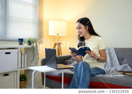 Smiling woman holding notebook while studying or working from home 130322938