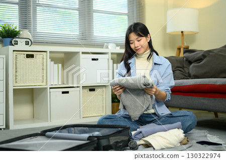 Traveler preparing for trip while folding clothes and packing suitcase on floor Traveler preparing for trip while folding clothes and packing suitcase on floor 130322974
