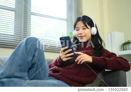 Young asian woman enjoys listening to music and browsing phone at home 130322983