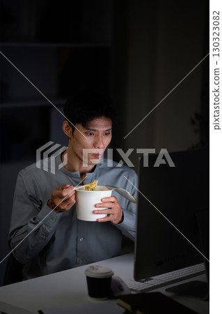 Man eating instant noodles while working late at computer 130323082