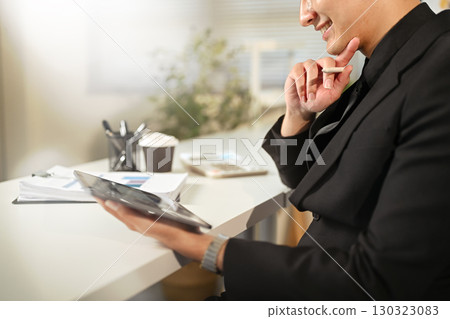 Smiling businessman in black suit using digital tablet at office desk 130323083