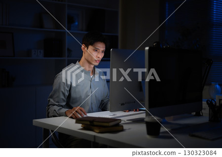 Businessman concentrates on his screen while working overtime at night 130323084