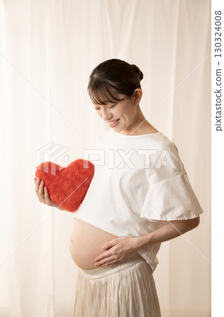 Eight-month pregnant woman holding a red heart 130324008