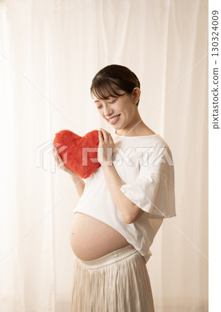 Eight-month pregnant woman holding a red heart 130324009