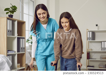 Young friendly nurse helping a child girl patient to walk with her crutches. 130324513