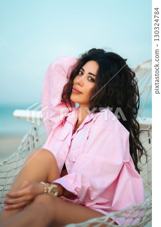 happy woman lying in hammock on sandy beach during vacation, joyful relaxation and tropical peace, cheerful girl resting on shore of resort at sunset 130324784