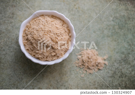 Overhead shot of nutritional yeast flakes in a small white bowl with small pile of flakes next to it on speckled background with copy space Overhead shot of nutritional yeast flakes in a small white bowl with small pile of flakes next to it on speckled background with copy space 130324907
