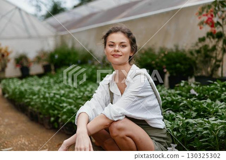 Young woman in a greenhouse, wearing a casual outfit, smiling amidst lush greenery, symbolizing a connection with nature and healthy living Young woman in a greenhouse, wearing a casual outfit, smiling amidst lush greenery, symbolizing a connection with nature and healthy living 130325302