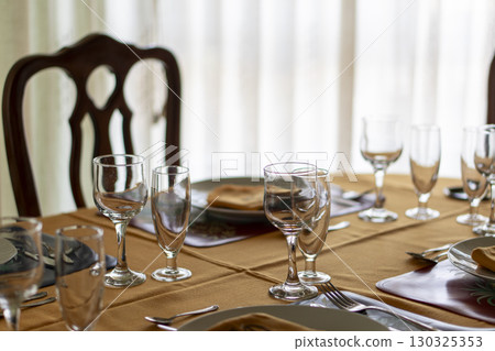 A table with a chair and a tablecloth with a few glasses and utensils A table with a chair and a tablecloth with a few glasses and utensils 130325353