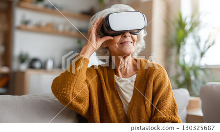 Concept of futuristic technology and fun from the elderly - Mature woman sitting on the sofa at home having entertainment and playing with virtual reality - Happy retired uses vr glasses 130325687