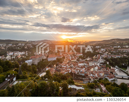 A breathtaking sunrise casts golden hues over Cesky Krumlov, illuminating its picturesque buildings and surrounding nature. The Vltava River flows gently, enhancing the magical landscape. 130326054