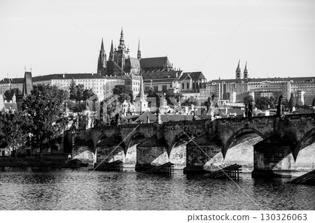 Picturesque skyline features Prague Castle towering above the historic Charles Bridge, while the Vltava River reflects their grandeur under a clear sky with no people around. 130326063