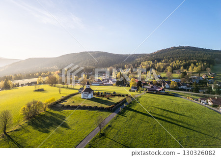 Tesarov Chapel stands out with its octagonal shape in Korenov, Jizera Mountains during a sunny day. The surrounding green fields and hills create a tranquil landscape. 130326082