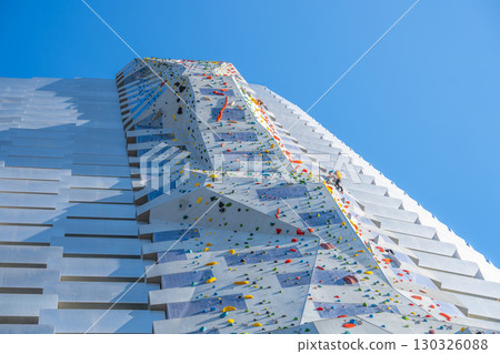 A climber ascends the Amager Bakke Climbing Wall, the highest climbing wall globally, located in Copenhagen, Denmark. Bright colors and dynamic angles create an exciting atmosphere. 130326088