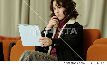 A young girl stretches her arms out, holding a notebook and pen with a determined expression. This image conveys themes of focus, creativity, and youthful energy in a casual setting. A young girl stretches her arms out, holding a notebook and pen with a determined expression. This image conveys themes of focus, creativity, and youthful energy in a casual setting. 130326104