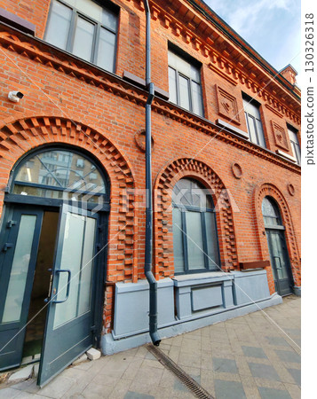 Detailed shot of an old red brick facade featuring arches and framed windows. The historic design emphasizes durability, symmetry, and urban aesthetic. Detailed shot of an old red brick facade featuring arches and framed windows. The historic design emphasizes durability, symmetry, and urban aesthetic. 130326318