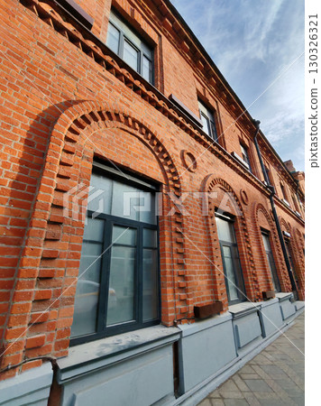 A vibrant red brick wall with arched window frames and decorative brick patterns. The shot captures the elegance of historic construction and urban restoration. 130326321