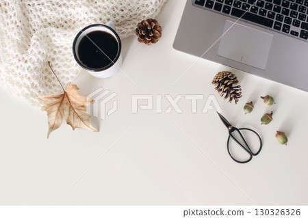 Autumn flatlay with laptop, coffee cup, knit blanket, pinecones, acorns, and dried leaf. Cup of coffee. Cozy workspace setup with neutral seasonal tones. Fall lifestyle, remote work concept. Top view. 130326326