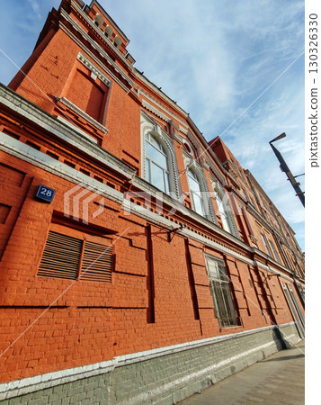 An ornate red brick structure with arched windows, white decorative elements, and shadows cast along its textured facade. The image showcases urban history and architectural craftsmanship. An ornate red brick structure with arched windows, white decorative elements, and shadows cast along its textured facade. The image showcases urban history and architectural craftsmanship. 130326330