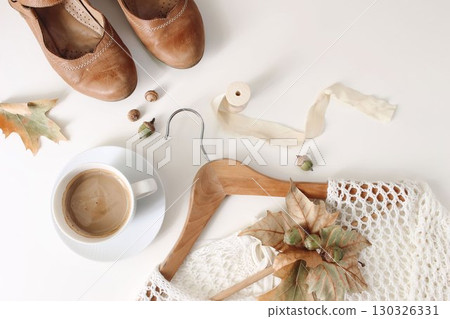 Autumn flatlay with leather shoes, coffee cup, wooden hanger, knitted sweater, acorns and dried leaves isolated on white background. Cozy fashion scene, neutral tones. Fall lifestyle composition, top Autumn flatlay with leather shoes, coffee cup, wooden hanger, knitted sweater, acorns and dried leaves isolated on white background. Cozy fashion scene, neutral tones. Fall lifestyle composition, top 130326331