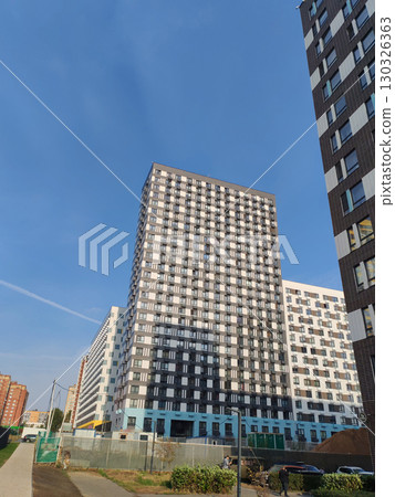 Two modern high-rise apartment buildings, one with a yellow and white facade, and the other with a dark and light checkerboard design. The contrasting geometric patterns reflect contemporary urban 130326363