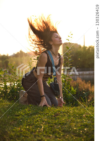 A woman, bathed in warm evening light, kneels by a peaceful lake, her expression open and sincere. The photo captures the essence of authenticity and the beauty of embracing one's vulnerability. 130326419