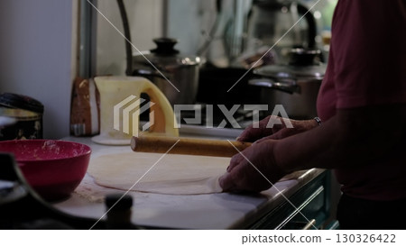 Wrinkled hands skillfully prepare dough on a floured surface, with kitchen utensils in the background. This moment captures the patience, love, and experience passed down through generations in home Wrinkled hands skillfully prepare dough on a floured surface, with kitchen utensils in the background. This moment captures the patience, love, and experience passed down through generations in home 130326422