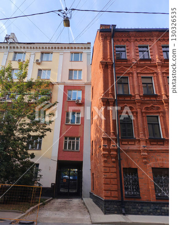 A richly detailed red brick facade with ornate arches, decorative balconies, and symmetrical black windows. The photo showcases urban heritage and classic architectural artistry. A richly detailed red brick facade with ornate arches, decorative balconies, and symmetrical black windows. The photo showcases urban heritage and classic architectural artistry. 130326535
