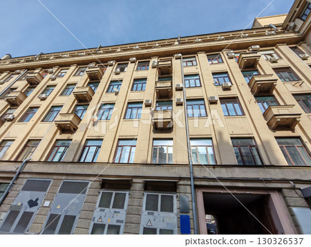 An upward view of a beige residential building with numerous windows, small balconies, and air conditioning units. The photo highlights urban density and the geometric symmetry of functional 130326537