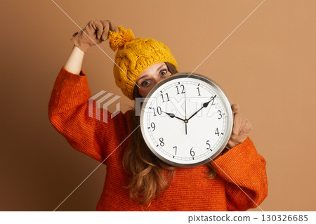 Playful Woman Peeks Over Wall Clock in Fall Attire Playful Woman Peeks Over Wall Clock in Fall Attire 130326685