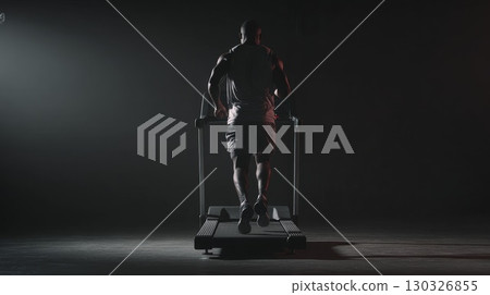 Determined male athlete running on treadmill in dark gym Determined male athlete running on treadmill in dark gym 130326855