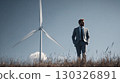 Businessman walking in field with wind turbine, investing in green energy 130326891