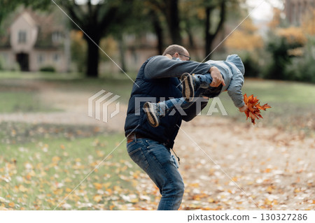 Autumn mood, a boy walking with his father and mother in an autumn village against the background of an old house and autumn trees, the boy holds a bouquet of maple leaves in his hands. Germany Autumn mood, a boy walking with his father and mother in an autumn village against the background of an old house and autumn trees, the boy holds a bouquet of maple leaves in his hands. Germany 130327286