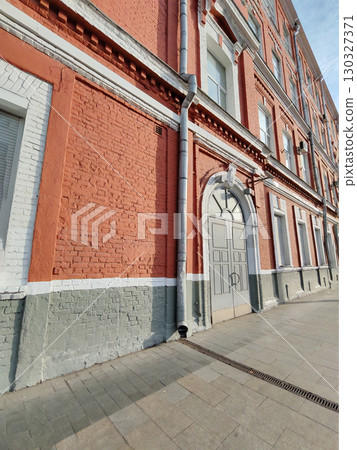 A vertical drainage pipe runs along a historic red brick wall with decorative white accents. This image showcases modern water management integrated into vintage architecture. A vertical drainage pipe runs along a historic red brick wall with decorative white accents. This image showcases modern water management integrated into vintage architecture. 130327371