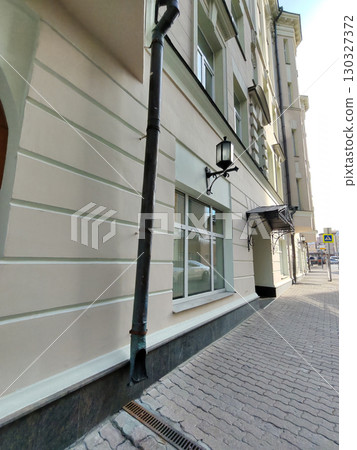 A beige building facade with decorative iron canopies, large wooden doors, and modern windows overlooking a brick-paved sidewalk. The image highlights architectural elegance and urban practicality. 130327372