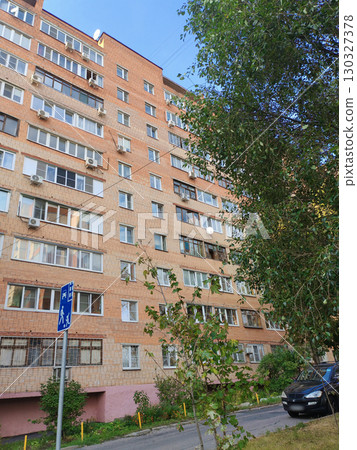 A tall red and beige brick residential building with multiple balconies, air conditioning units, and a sidewalk below. The structure reflects the typical architecture of urban apartment blocks in A tall red and beige brick residential building with multiple balconies, air conditioning units, and a sidewalk below. The structure reflects the typical architecture of urban apartment blocks in 130327378