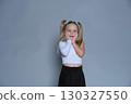 This little girl poses with a cute, surprised expression, her hands resting on her cheeks. The studio setting and fashionable outfit add to the charm of the moment, making it ideal for children s 130327550