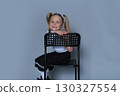 A happy 5-year-old girl, dressed in a stylish skirt and boots, is captured laughing while leaning on a chair in a studio setting. The photo showcases her playful side, perfect for children's 130327554