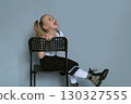 joyful 5-year-old girl laughs playfully while sitting backwards on a black chair during a studio photo session. Her lively expression and stylish outfit highlight her personality, making this photo 130327555