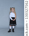 young girl with blonde pigtails is standing confidently against a grey background, wearing a stylish one-shoulder white top, a black pleated skirt, white lace socks, and black boots. Her pose is 130327562