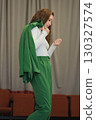 A composed individual wearing a vibrant green outfit, her stance and expression reflecting contemplation and grace. 130327574