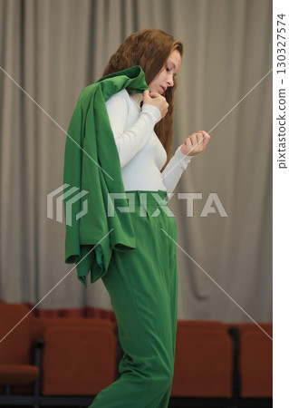 A composed individual wearing a vibrant green outfit, her stance and expression reflecting contemplation and grace. 130327574