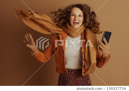 Energetic Woman Jumps with Smartphone in Autumn Attire 130327734