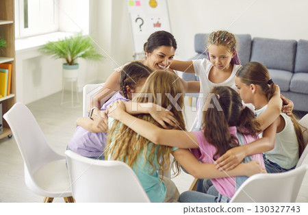 School girls sitting in a circle and hugging with psychologist woman during therapy session. 130327743