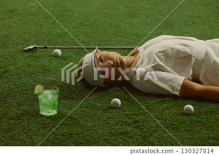 Woman golfer lying on grass with lime cocktail golf balls and club serene expression Woman golfer lying on grass with lime cocktail golf balls and club serene expression 130327814